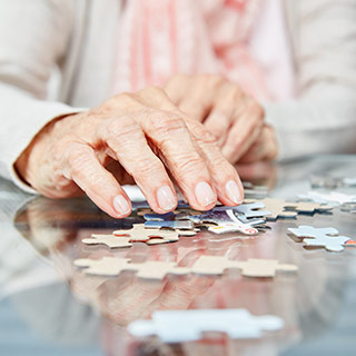Hände einer älteren Person beim Zusammensetzen eines Puzzles